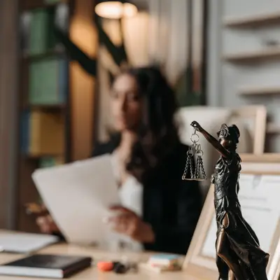 Lawyers sitting at her desk on a blurred background, foreground is the Lady Justice statue in bronze.